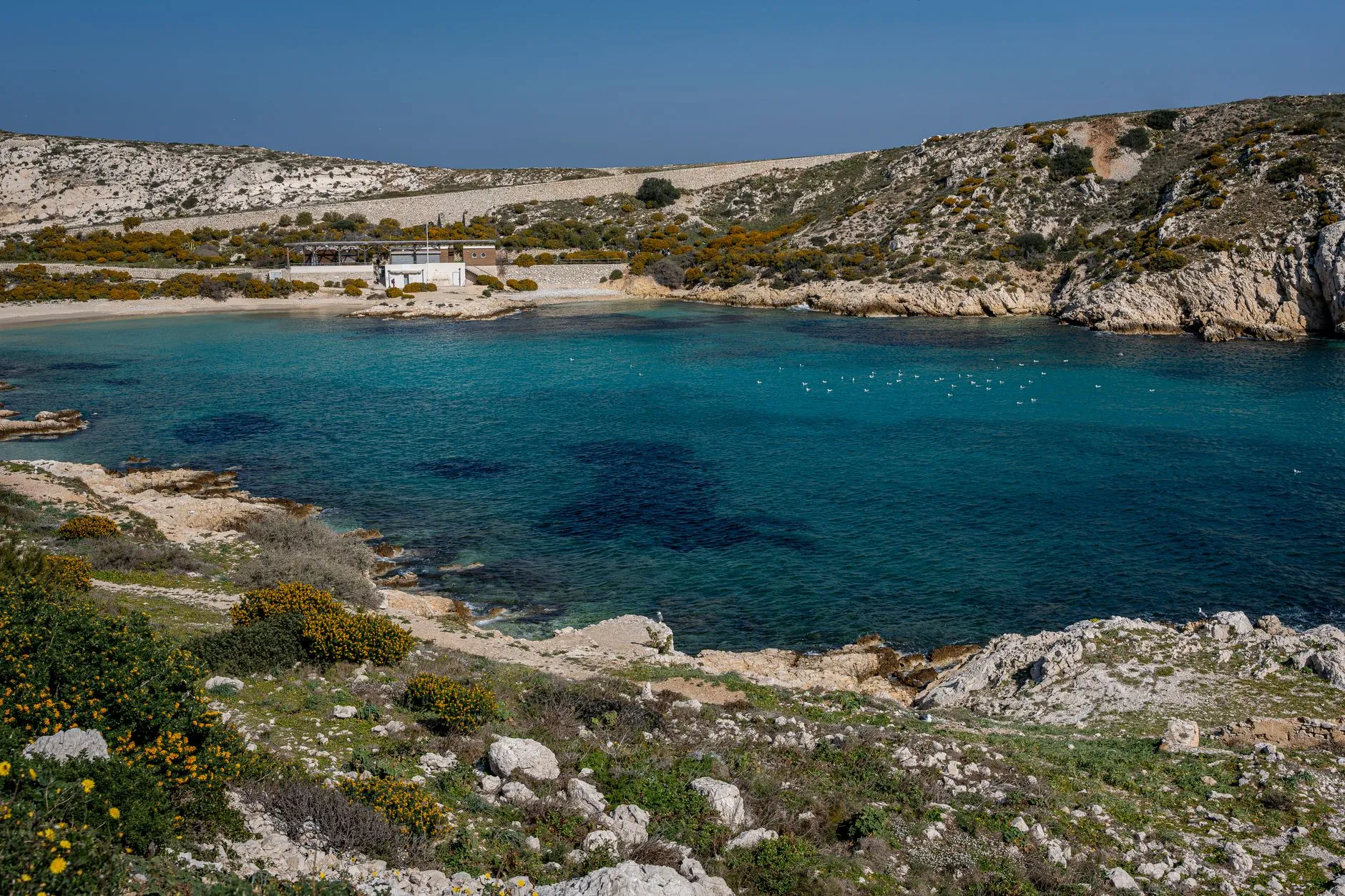 Explore this tranquil bay with turquoise waters, rocky hills, and a serene beach house.